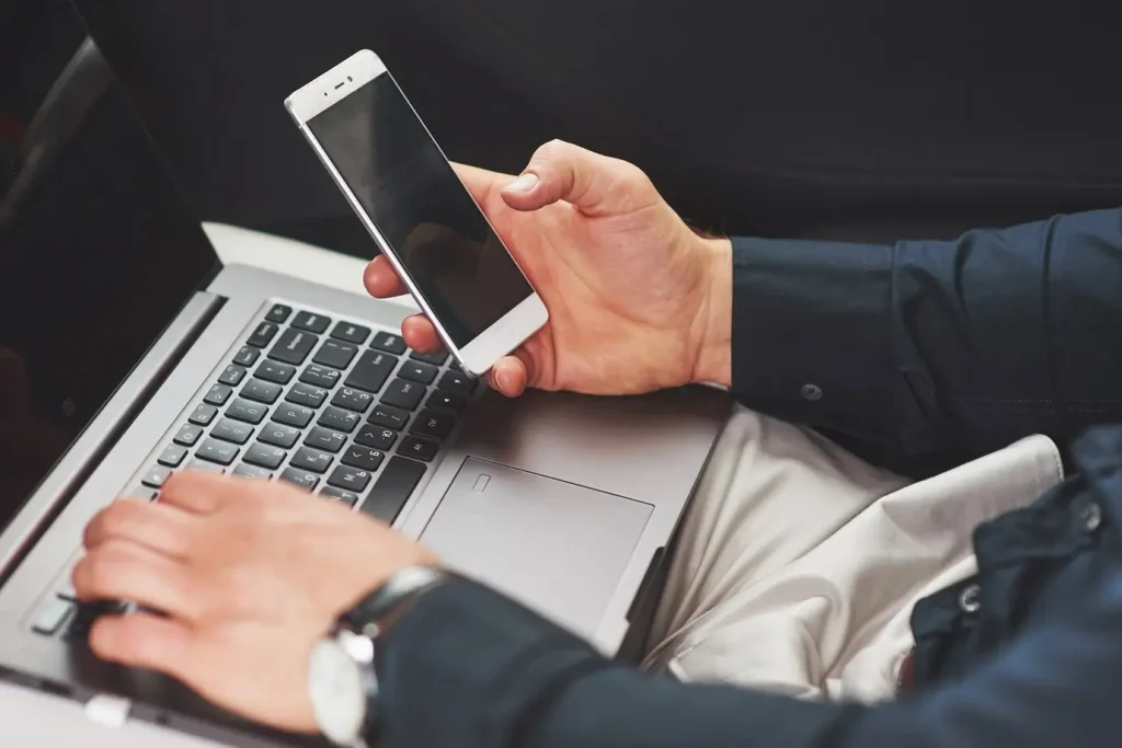 A photo of a man using a mobile phone and laptop computer for online banking with a credit union. Better Lobby software platform allows members to add themselves to an online queue. Better Lobby also has a mobile booking tool, where members can book appointments using their phone or laptop.