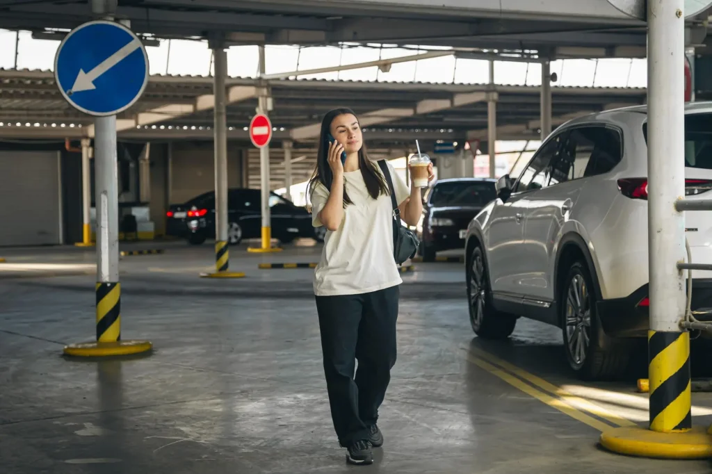 A photo of a person on their phone in the parking lot. Members of Credit Unions can use the online queue to plan their visit to the credit union before travel to the branch, able to see wait times or number of members waiting at the branch. When members arrive they can do a parking lot check in, where they can add themselves to the credit union queue from the parking lot.